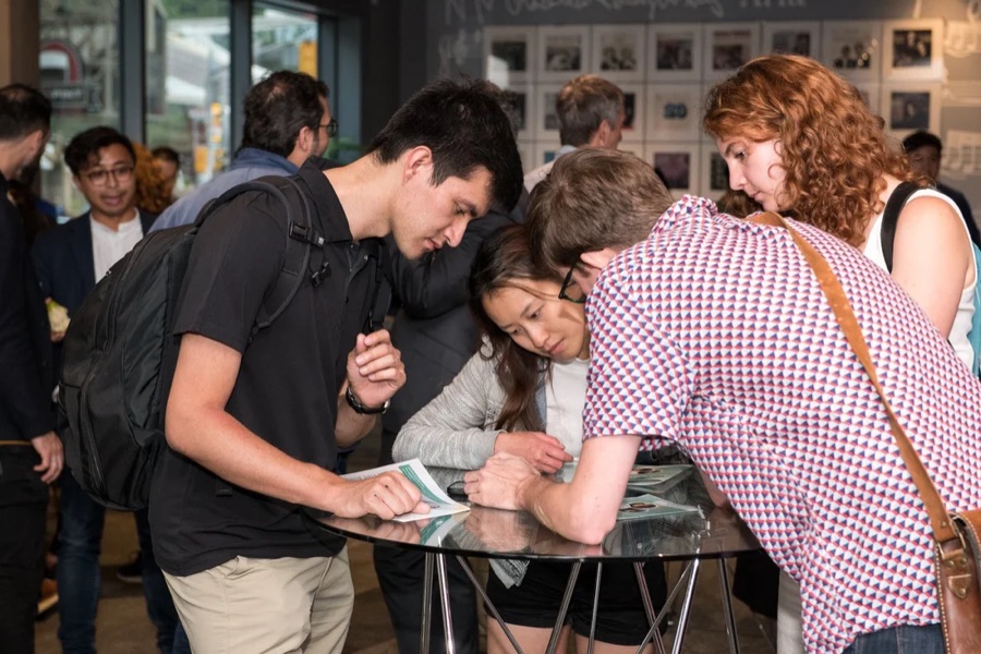 Conference attendees leaning over a table together, mid-conversation.