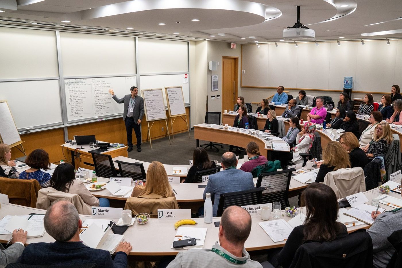 Misha leading a workshop in a tiered classroom, with notes on whiteboards behind him.