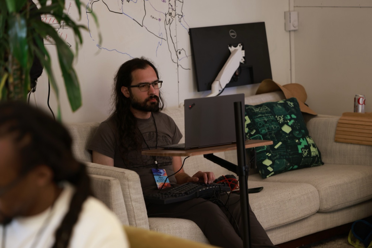 An attendee on a sofa working at a laptop, in front of a whiteboard wall covered in a hand-drawn map.